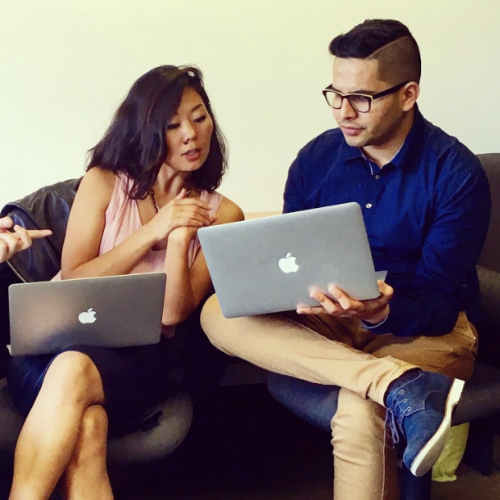 Two international internship students talking and looking at their laptops